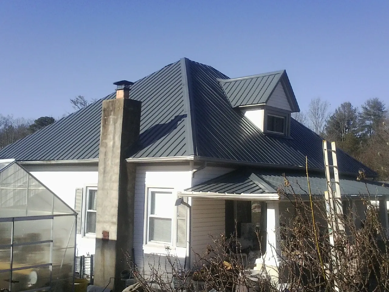 Dark blue standing seam metal roof on a white farmhouse with dormer — Slate & Tile Roof Repair by Roofing Brothers in Wilber