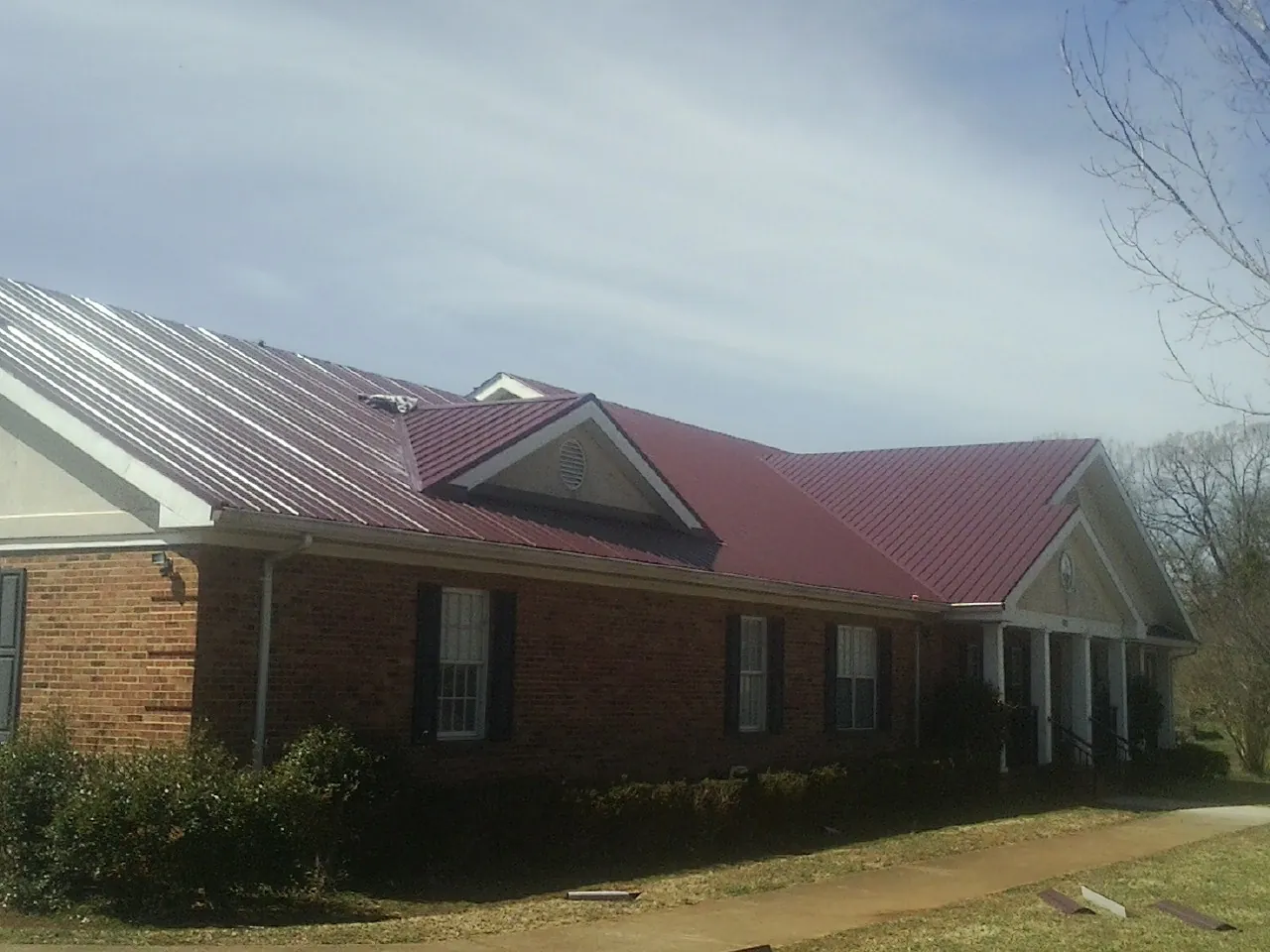 Red metal roof with gabled entries on a long brick building, from a Hail Damage Roof Repair job in Wilber