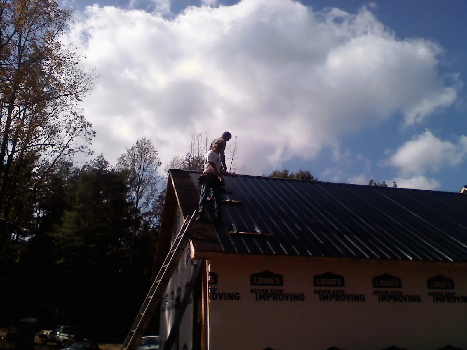 Roofer fastening dark metal panels high against a cloudy sky, from a Roof Inspection job in Wilber