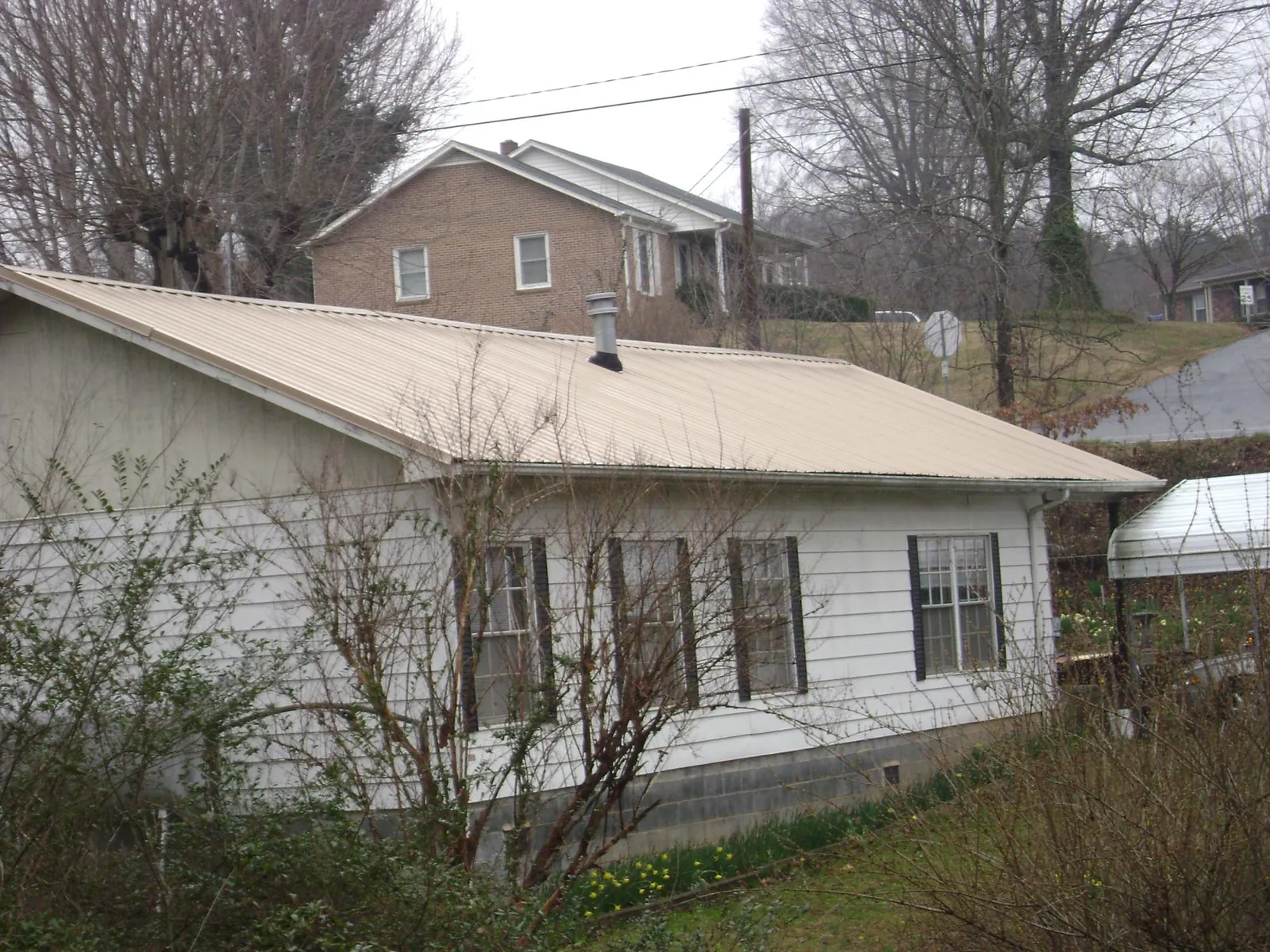 Tan metal roof on a white sided house set into a hillside — Commercial Roofing by Roofing Brothers in Wilber