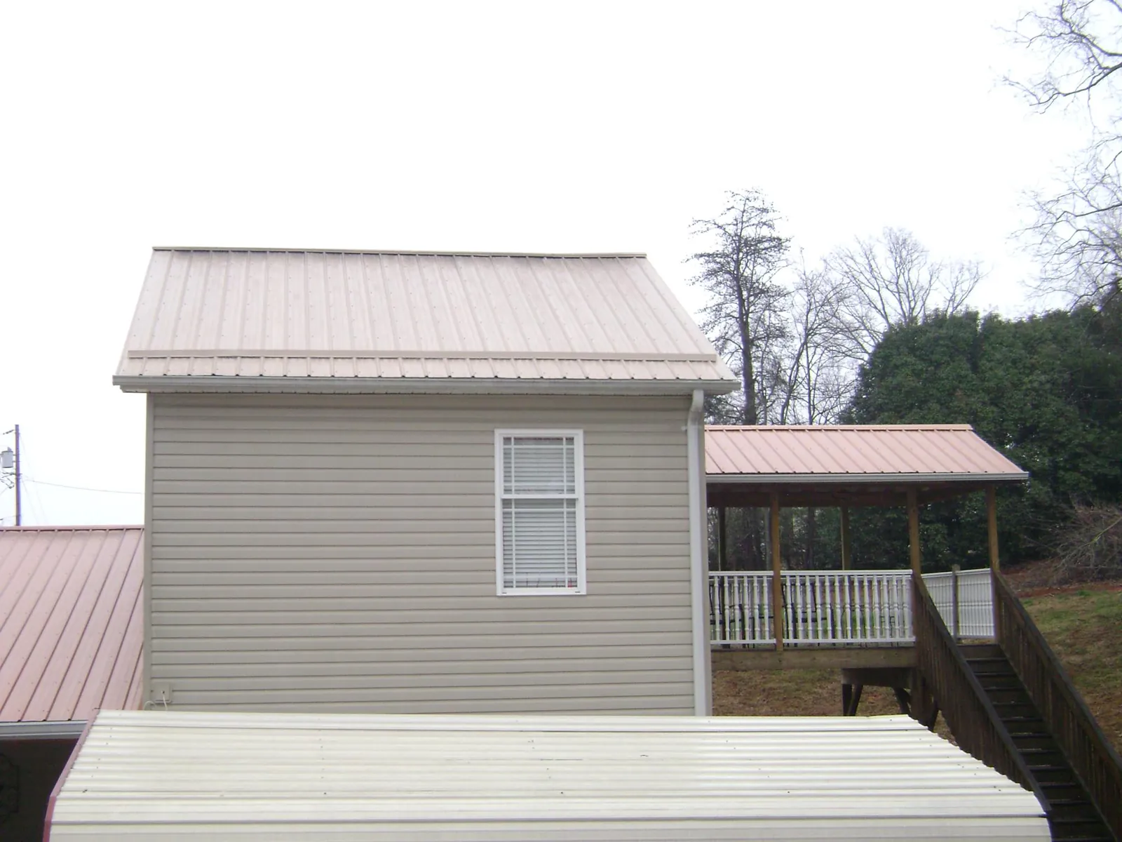 Tan metal roofs on a two story addition and attached porch, from a Roof Replacement job in Wilber