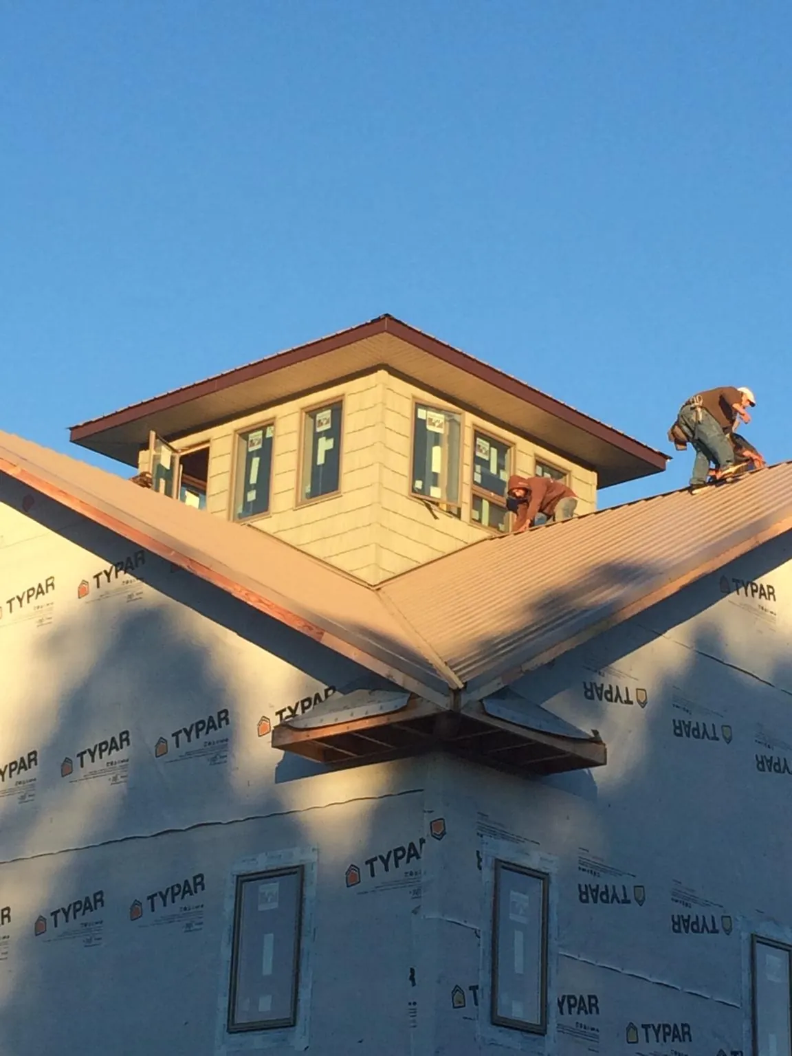 Roofers working around a rooftop cupola on a new metal roof at sunset — Roof Waterproofing in Wilber by Roofing Brothers